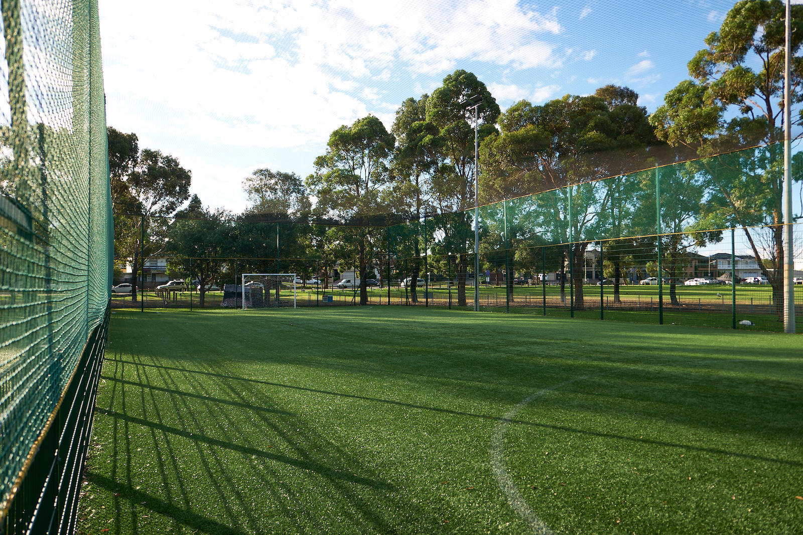 A pair of flat-soled trainers, slim shin pads and a water bottle laid out on the sideline of a caged pitch at KIKOFF Northern Beaches.