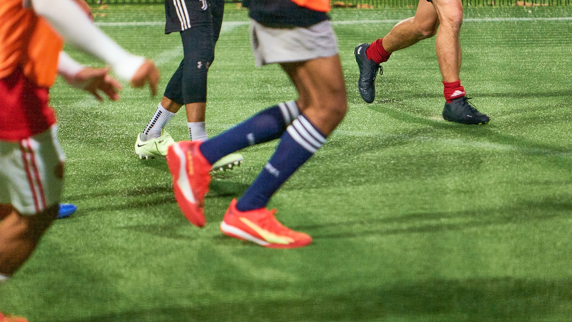 Kids playing a small-sided game on a floodlit caged synthetic pitch at a KIKOFF venue.